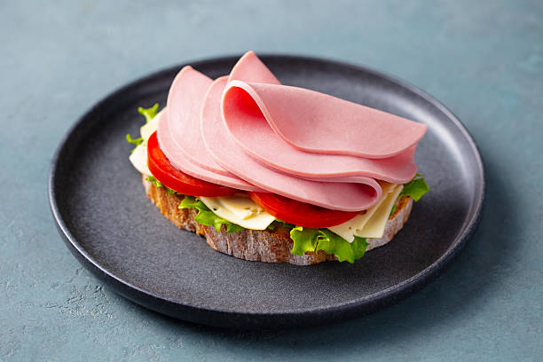 istock Fresh sandwich with ham, cheese, lettuce and tomato on rustic bread, served on a dark plate. Grey background. Close up. 2246700520