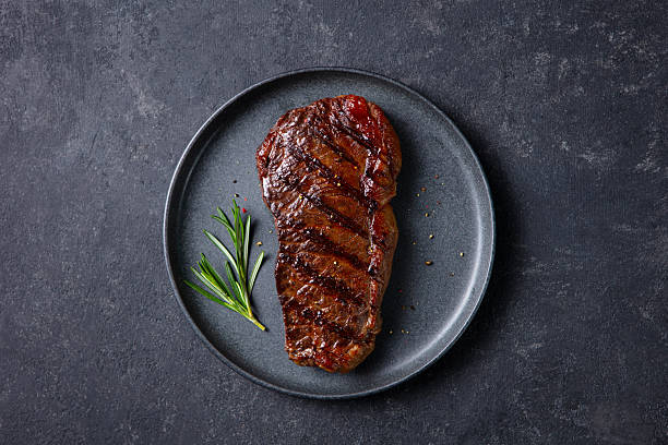 istock Grilled steak served on dark plate, enhanced with rosemary touch. Dark grey background. Close up. Top view. 2246700848
