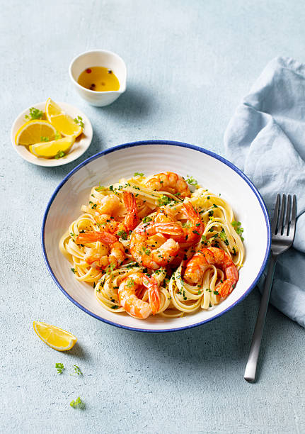 Delicious shrimp pasta dish with lemon accents and fresh herbs. Light blue background.