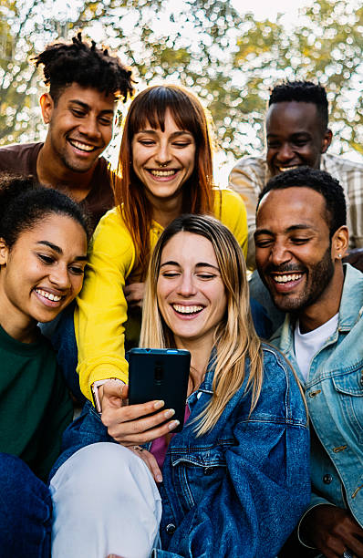 istock Young happy friends having fun together using mobile phone sitting outdoors 2246701509