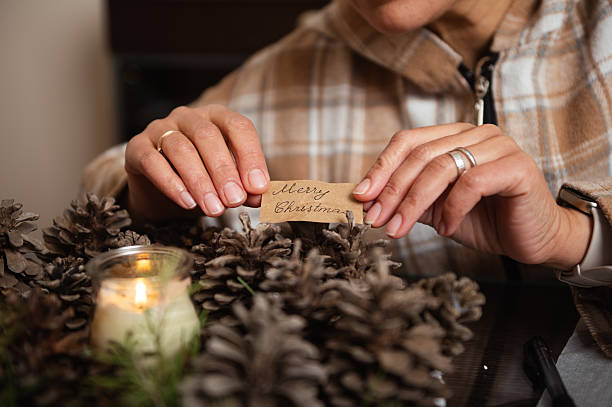 Hands Place A Merry Christmas Tag Among Pine Cones In Rustic Cozy Home Decor