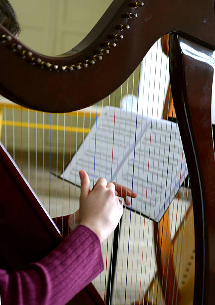 Close-up of a young harpist's hands plucking the strings of her harp, a musical score visible in the background