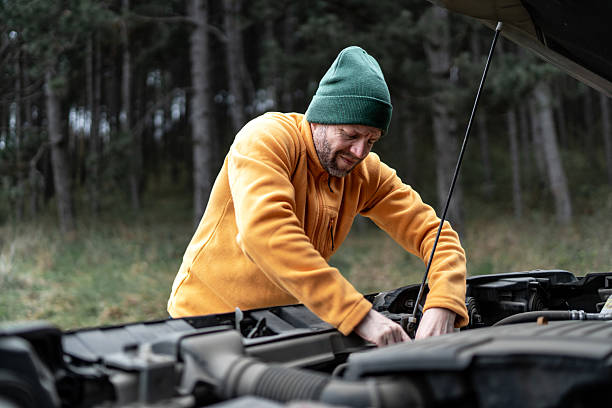 istock Man trying to repair broken down car engine in forest 2246722325