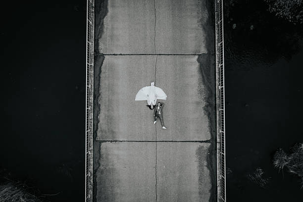 Person reclines on a bridge with an umbrella, surrounded by dark water and grass, evoking a tranquil yet dramatic ambiance in a black and white scene