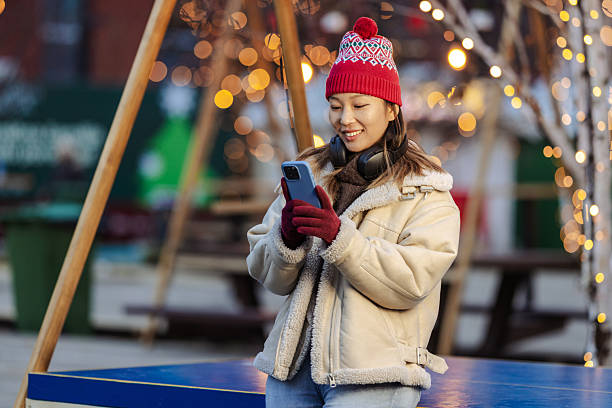 istock Young woman at a festive winter market, smiling while using her phone under twinkling lights 2246728633