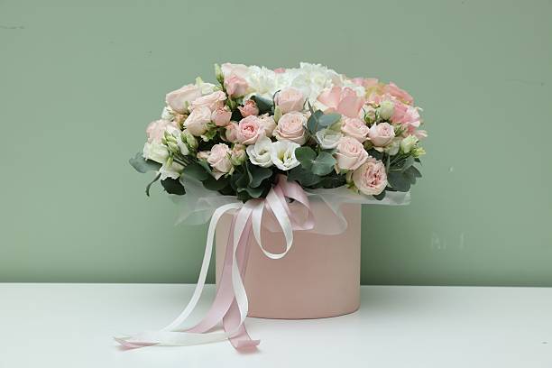 istock Gift box with bouquet of beautiful flowers and eucalyptus branches on white table against green background 2246729756