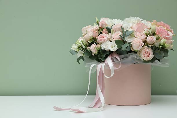 istock Gift box with bouquet of beautiful flowers and eucalyptus branches on white table against green background. Space for text 2246729758
