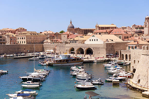 Dubrovnik, Croatia, June 30, 2025: A view of small boats moored in the old harbor beside the historic stone walls and bright waterfront buildings. Concept of travel journalism, urban reportage.