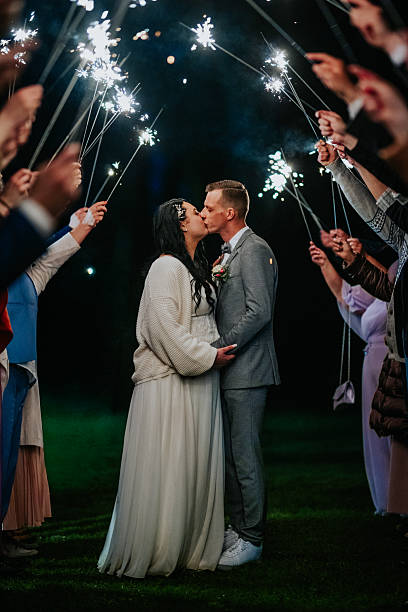 istock Bride and groom share a romantic kiss surrounded by guests holding sparklers, creating a magical atmosphere during a nighttime wedding celebration with glowing lights 2246733519