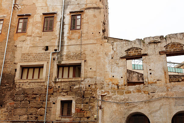 A weathered brick and stone facade shows crumbling architecture and exposed piping along a worn urban wall. The scene captures decay, history, and the texture of rustic construction for architectural and urban stock imagery.