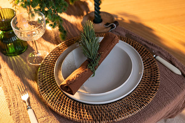 istock Festive table setting with woven charger, ceramic plates, rustic napkin and greenery decoration in warm holiday lighting. 2246734404