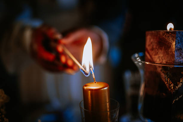 istock Individual lighting a golden candle with a matchstick, creating a warm glow in a dimly lit environment, surrounded by decorative elements and a cozy atmosphere 2246735220