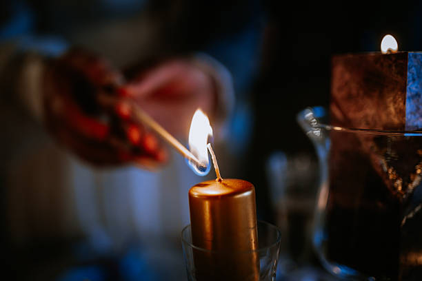 istock Individual lighting a golden candle with a matchstick, creating a warm glow in a dimly lit environment, enhancing the ambiance of a cozy evening setting 2246735716