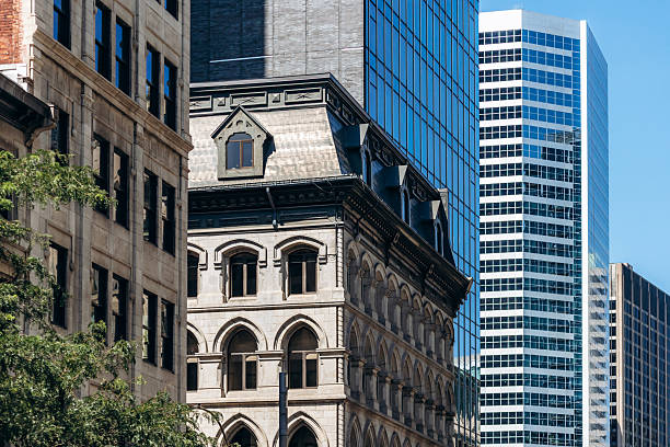 Montreal, Canada - August 11, 2025: Historic stone building with arched windows surrounded by modern glass skyscrapers in downtown Montreal