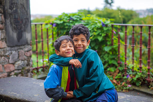 Two smiling brothers share a warm embrace while sitting outdoors on a cloudy day.