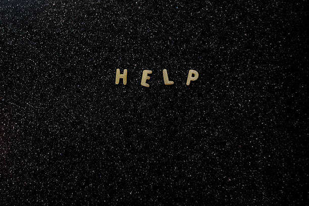 Small pasta letters spelling “HELP” are arranged on a dark, speckled surface, creating a simple yet striking composition with strong contrast and minimalistic design