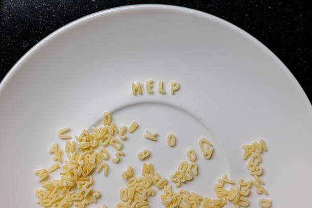Alphabet pasta letters arranged to spell “HELP” on a white plate, surrounded by scattered noodles, creating a playful yet expressive composition against a contrasting dark background