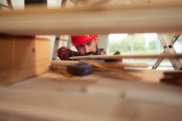 Focused construction worker wearing a red helmet building the wooden framework of a house under construction with daylight providing natural lighting