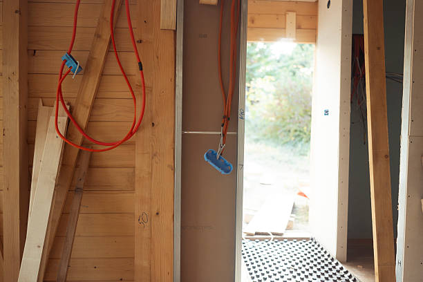 Interior of a wooden house under construction showing unfinished walls with exposed electrical wiring and natural light entering through an open doorway during daytime