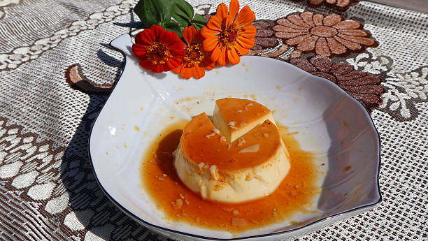 istock Part 3: A Mini Caramel Pudding Ready to Eat With Syrup-Filled Orange Top and Spoon, Set Against Three Vibrant Red & Orange Zinnia Flowers. 2246765917