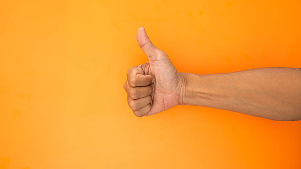 istock Hand giving a strong thumbs up gesture against a vibrant orange wall. 2246774169