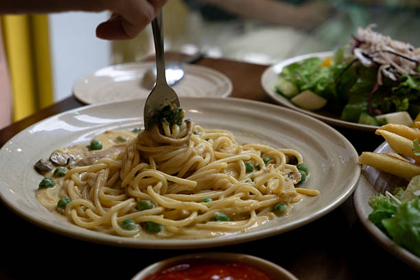 Creamy pasta with peas being twirled on a fork, served alongside a fresh salad and crispy fries.