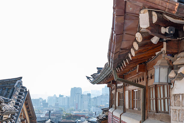Close-up of traditional Korean hanok wooden roofs with curved tiles and eaves. Historic architecture contrasts with modern city skyline in background. Cultural heritage and urban landscape.