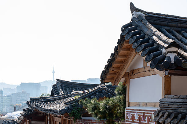Close-up of traditional Korean hanok roofs with detailed tiles and wooden beams. Historic architecture contrasts with modern city skyline in the background. Cultural heritage and urban landscape.