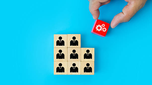 istock Hand choosing cog with people on cube wooden toy block stack. Concepts of ideas creative thinking or human resources personnel leader or leadership or business team player performance. 2246779003