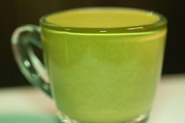 Super macro emphasizing reflections and highlights from the glossy surface of matcha latte inside a glass.