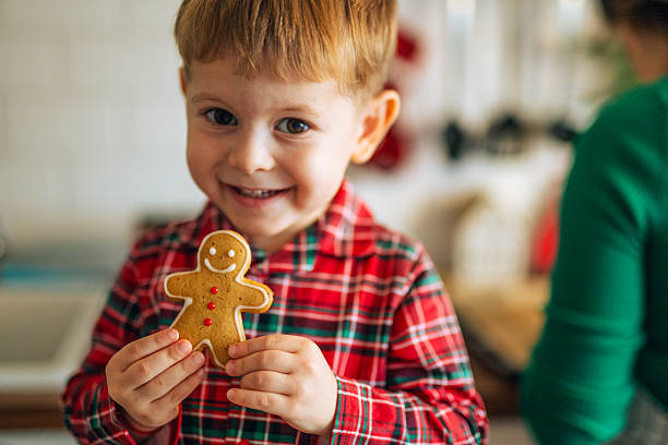 Cute shot of a boy toddler eating freshly baked gingerbread Christmas cookia at home.