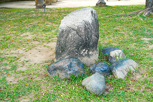 A group of decorative stones placed on a green lawn in a public park, featuring a tall textured rock with painted details. Clear natural lighting reveals surface textures, ideal for landscape design, garden décor, and outdoor environmental themes.