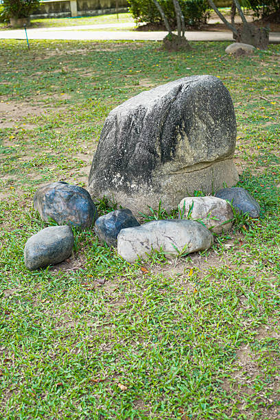 A decorative rock formation consisting of a large painted stone and smaller rocks arranged on a grassy lawn in a public park. Natural daylight highlights textures and placement, suitable for nature backgrounds, garden decoration, and landscape elements.