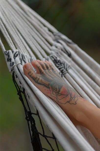 A close-up of a foot resting in a hammock, showcasing a colorful tattoo against a tranquil background, ideal for relaxation and wellness themes.