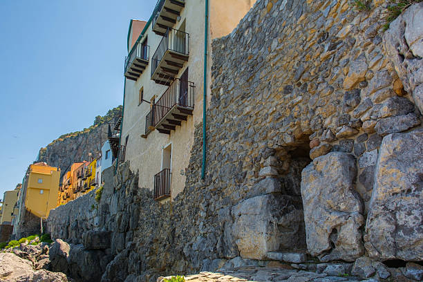 Part of the ancient sea walls of Cefalu in Sicily, Italy. The walls were constructed as polygonal masonry, also called megalithic or cyclopean, & date back to 5th-4th century BC, representing Cefalu's oldest architectural layer. Perched atop are historic houses, their foundations merging with the ancient walls. A postern gate, or a secondary gate, provided direct access to the rugged calcarenite limestone coast for fishermen & for defence