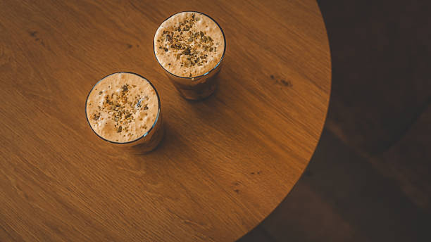 Close-up of a man's hand holding an iced coffee in a jar with a bamboo straw. Wrapped sandwich on a woven placemat. Cozy cafe atmosphere.