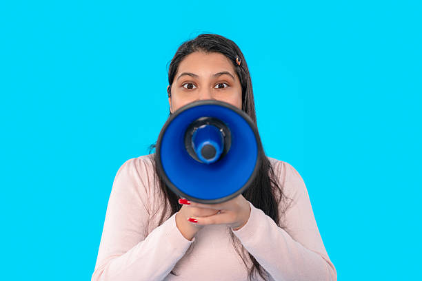 istock Woman holds megaphone against bright blue background during announcement 2246838564