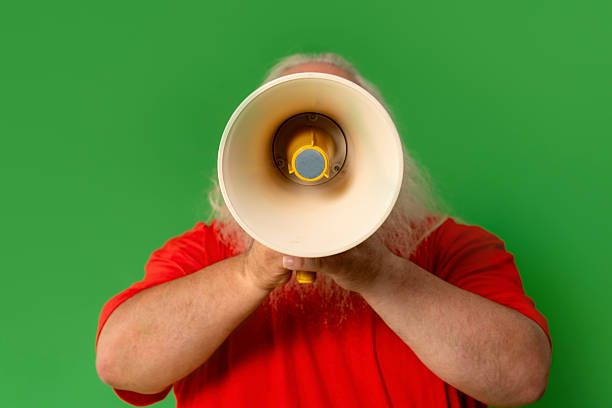 istock Confident man in red shirt speaks into megaphone against green backdrop 2246838808