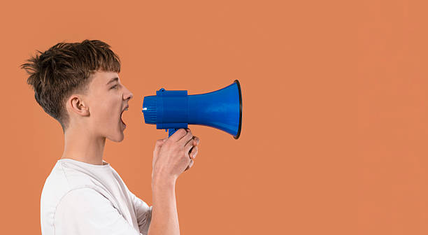 istock Young person shouts into blue megaphone against orange background 2246839941