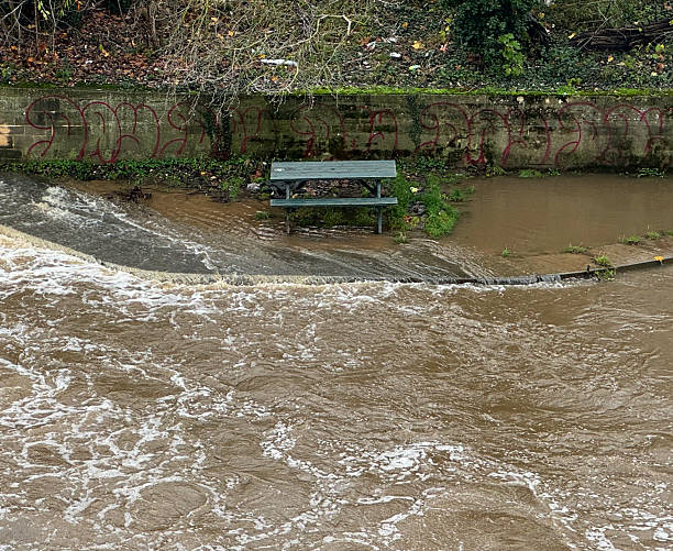 Green wooden picnic bench on the banks of the Avon in Bath, Somerset after heavy rain