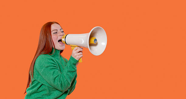 istock Woman uses megaphone against bright orange background during lively protest 2246841248