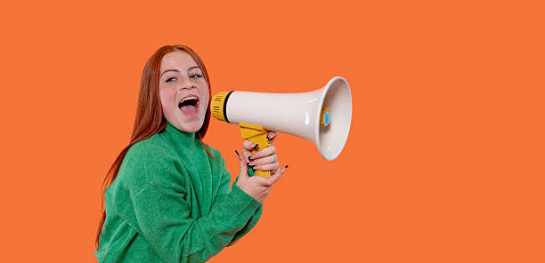 istock Young woman enthusiastically using a megaphone against a bright orange backdrop 2246841252