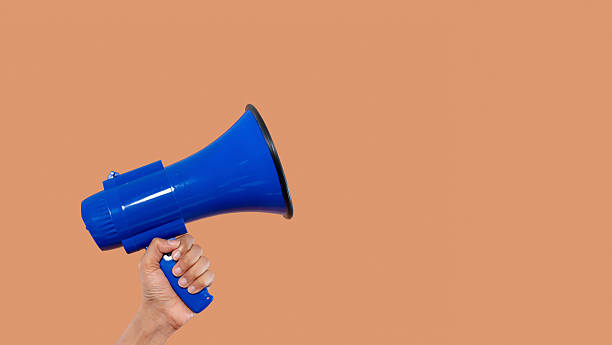 istock Blue megaphone held in hand against a simple background 2246841428