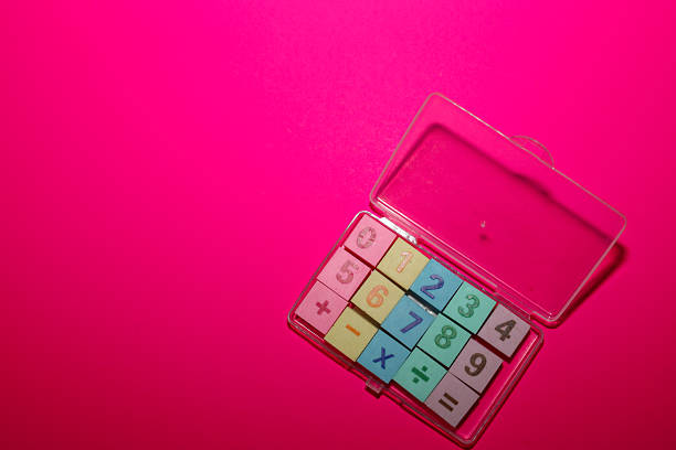 A vibrant magenta background provides a saturated backdrop for a clear plastic case, open and filled with small square tiles of numbers and symbols.