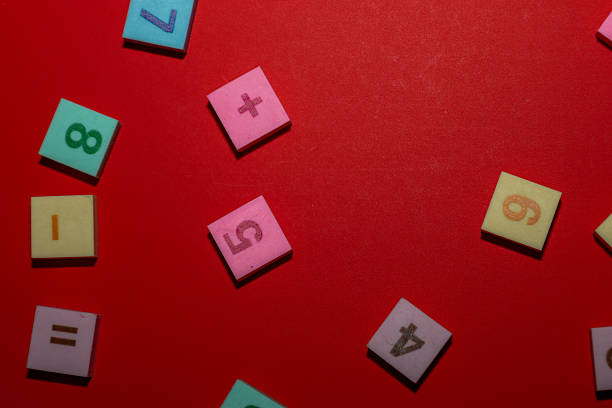 istock A deep red background serves as a contrasting canvas for a sparse scattering of multi-colored square tiles. These tiles feature embossed numbers 1, 4, 5, 6, 7, 8, plus symbols for addition and equality, creating an engaging yet minimalist educational visu 2246848046