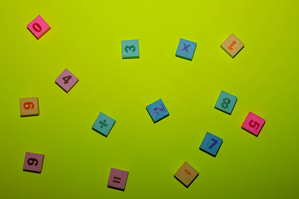 This top-down shot showcases a scatter of multi-colored square tiles featuring embossed numbers and mathematical symbols against a bright lime-green background.