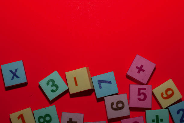 istock ​A vibrant red background dominates this shot, providing bold copy space, while colorful square tiles cluster along the bottom of the frame. The tiles feature embossed numbers, including 1, 2, 3, 5, 7, 8, 9, plus multiplication and addition symbols, 2246848058