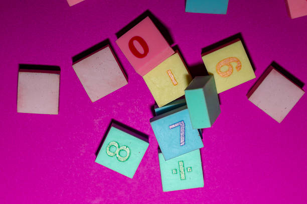 This top-down shot showcases a scatter of multi-colored square tiles, used for games or education, on a vibrant magenta background. The tiles feature various embossed numbers like 0, 1, 6, 7, 8, and a division symbol, creating an engaging visual element.