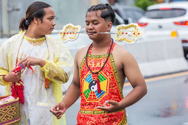 Phuket, Thailand - November 06 2025: Two participants in the annual Vegetarian Festival parade in Phuket, Thailand. One devout follower performs ritualistic cheek piercing with an elaborate skewer,