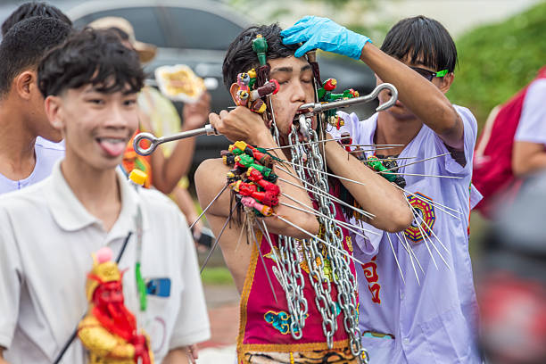 Phuket, Thailand - November 06 2025: Devotee endures extreme self-mortification with skewers, spears, and chains piercing his face and body during the vibrant Phuket Vegetarian Festival. A powerful